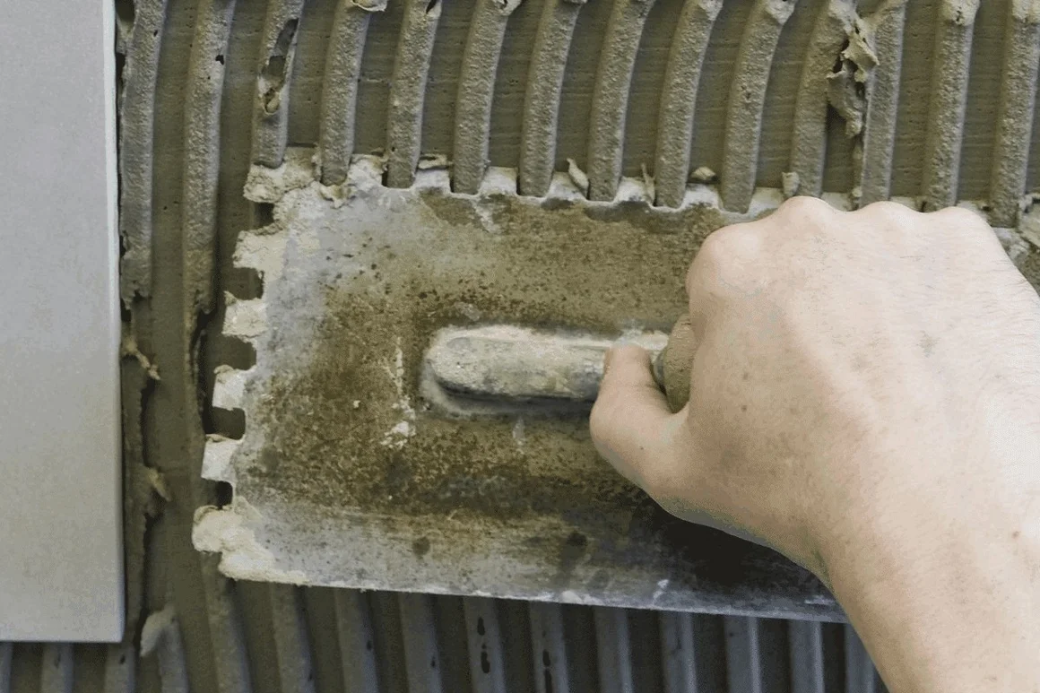 Hand verteilt Fliesenkleber mit Zahnspachtel